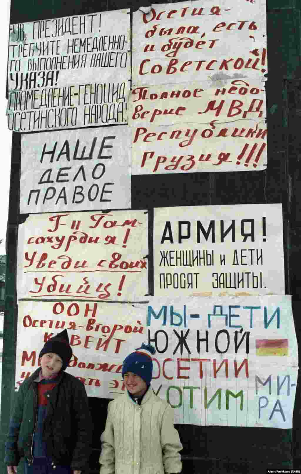 Діти в Цхінвалі 1 січня 1991 року позують поруч із плакатами на пам&#39;ятнику Леніну, який осетини не дозволили знести. На одному з плакатів написано: &laquo;Осетія була, є і завжди буде радянською!&raquo; Багато грузинів вважали етнічних осетин зрадницькою &laquo;п&#39;ятою колоною&raquo; в той час, як їхня країна боролася за свободу від Радянського Союзу. А осетини відчували себе відстороненими від нових законів, які зробили грузинську мову єдиною офіційною мовою країни і перешкоджали політичному представництву осетин в Тбілісі 